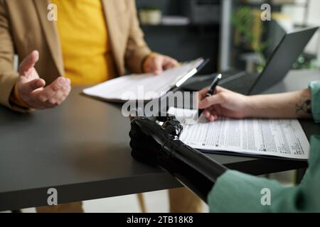 Close-up of woman with prosthetic arm filing medical documents during meeting with consultant in office Stock Photo