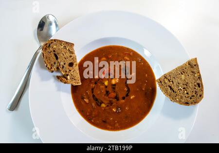 Bean and tomato soup with healthy seeded brown bread in a white bowl Stock Photo