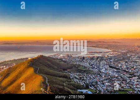 cape town aerial panorama from the table mountain at sunset, sun shining on the mountain range , few ships in the port unloading, industrial, town in Stock Photo