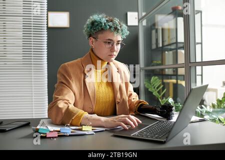 Serious businesswoman with disability concentrating on her online work on laptop in office Stock Photo