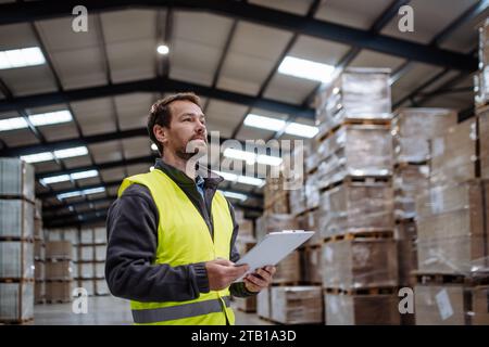 Portrait of warehouseman with clipboard checking delivery, stock in warehouse. Warehouse worker preparing products for shipment. Stock Photo
