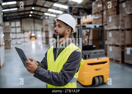 Warehouseman with tablet checking delivery, stock in warehouse. Warehouse manager using warehouse management software, app. Stock Photo