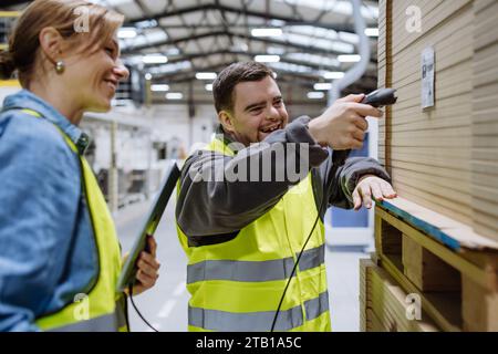 Young man with Down syndrome working in warehouse, female colleague teaching him scan products with scanner. Concept of workers with disabilities Stock Photo