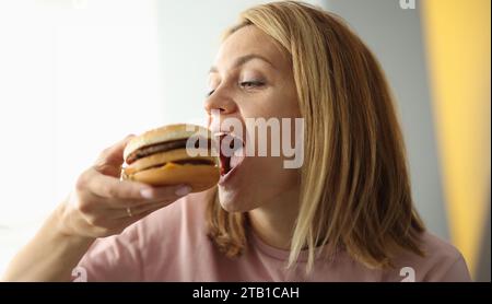 Young woman bites her mouth wide open hamburger Stock Photo