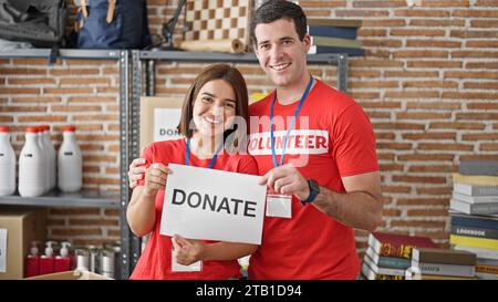 Man and woman volunteers standing together holding paper with donate message at charity center Stock Photo