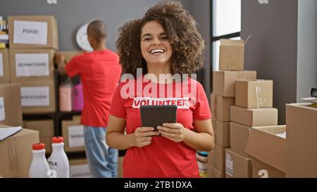 Smiling man and woman volunteers using touchpad together at charity center, strengthening community through altruism and digital activism Stock Photo