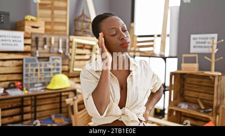 Stressed african american woman carpenter battling troublesome headache in busy carpentry workshop Stock Photo