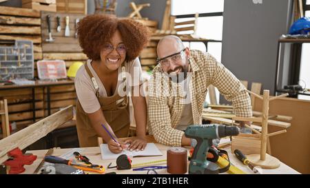 Two smiling carpenters confidently taking notes in their woodworking workshop Stock Photo