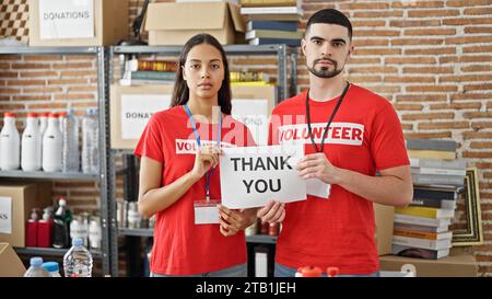 Man and woman volunteers standing together holding thank you paper at charity center Stock Photo