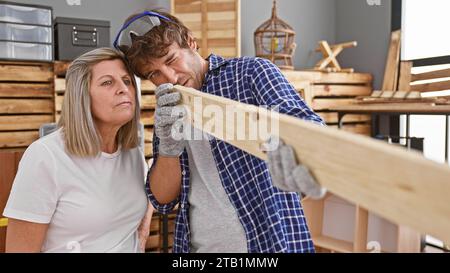 Two pro carpenters, man and woman, together looking at timber plank, giving a thumbs-up gesture, signalling 'ok' in their carpentry studio Stock Photo