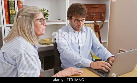 Two hardworking office workers, a man and a woman, together intensely working on a laptop, projecting the image of an unstoppable team. Stock Photo