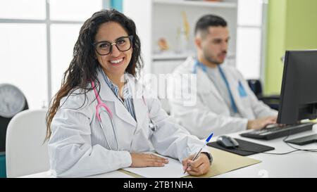 Man and woman doctors using computer taking notes smiling at the clinic Stock Photo