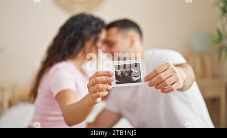 Man and woman couple sitting on bed holding baby ultrasound at bedroom Stock Photo