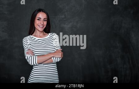 Close up photo of smiling cute happy young woman standing against blackboard in casual wear Stock Photo
