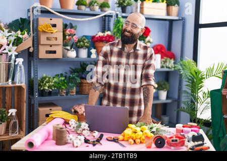 Young bald man florist smiling confident using laptop at flower shop Stock Photo