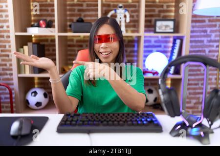 Middle age chinese woman wearing virtual reality glasses amazed and smiling to the camera while presenting with hand and pointing with finger. Stock Photo