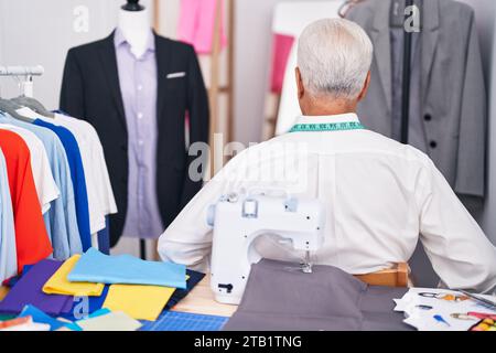 Middle age man with grey hair dressmaker using sewing machine standing backwards looking away with arms on body Stock Photo