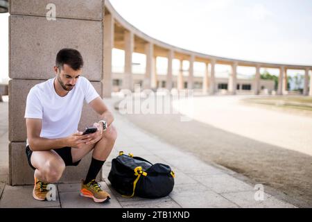 Young fitness man runner texting with a sports bag. Stock Photo