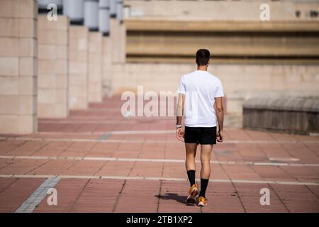 Back view of a relaxed fit runner man walking outdoors. Stock Photo