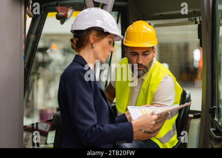 Forklift driver talking with manager in modern industrial factory. Warehouseman reading order, order picking. Warehouse worker preparing products for Stock Photo