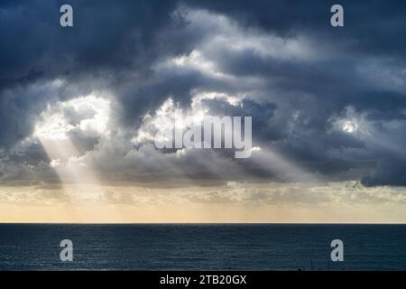 Rays of sun shining through storm clouds onto ocean. Stock Photo
