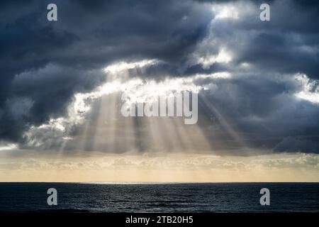 Rays of sun shining through storm clouds onto ocean. Stock Photo