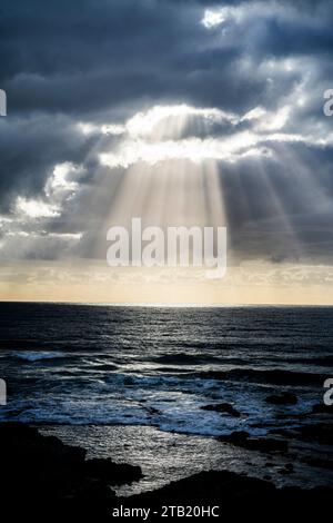 Rays of sun shining through storm clouds onto ocean. Stock Photo