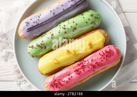 Various glazed sweet eclairs with with berry tastes closeup on plate on wooden background. Horizontal top view from above Stock Photo