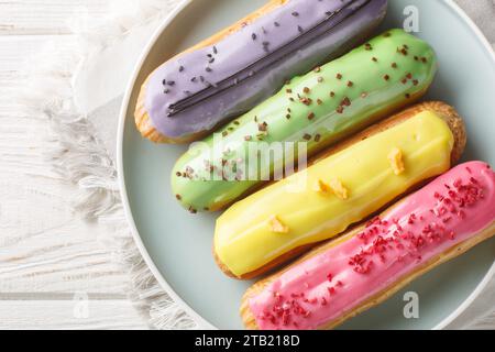 Multi-colored berry eclairs with lemon, pistachio, raspberry and blueberry flavors close-up in a plate on a wooden table. Horizontal top view from abo Stock Photo