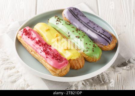 Various glazed sweet eclairs with with berry tastes closeup on plate on wooden background. Horizontal Stock Photo