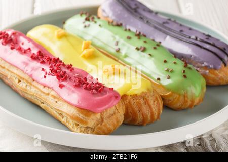 Multi-colored berry eclairs with lemon, pistachio, raspberry and blueberry flavors close-up in a plate on a wooden table. Horizontal Stock Photo