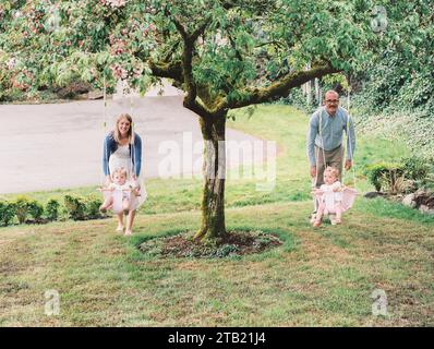 Parents enjoy outdoor family time, pushing their twin baby daugh Stock Photo