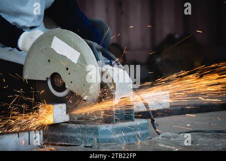 Heavy Industry Engineering Factory Interior with Industrial Worker Using Angle Grinder and Cutting a Metal Tube. Cutting metal and steel with a combin Stock Photo