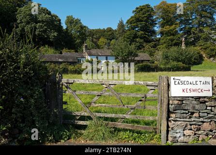 Old wooden farm gate and cottage near to a stone direction sign for Easedale Tarn and Keswick in summer Grasmere Cumbria England UK United Kingdom GB Stock Photo