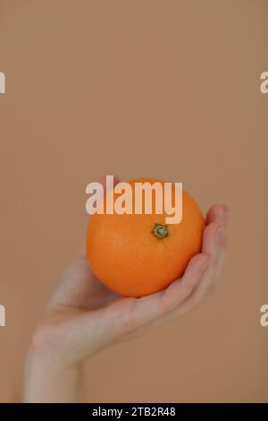 hand holds a fresh tropical orange. An orange in a woman's hand on a yellow background isolated. Girl holding a citrus in one hand Stock Photo