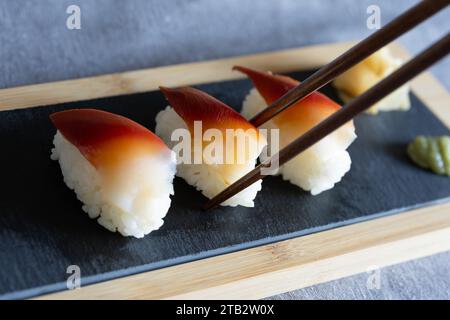 Chopsticks holding a piece of surf clam sushi (edible saltwater clam, Japanese: hokki gai) - homemade Japanese style food on a slate board Stock Photo