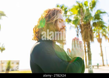 handsome redhaireb man with long beard wear black sporty suit doing yoga meditation in sunny beach Stock Photo