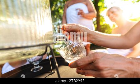 Close-up of hand pouring water from a dispenser with people in the background Stock Photo