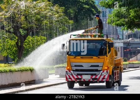 Truck with a water tank waters plants and flowers from a fire hose, a city park worker. Stock Photo