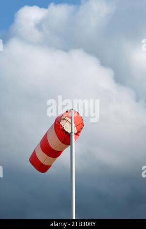 A red and white striped windsock on a pole against a cloudy and stormy sky. Image with copy space. Stock Photo