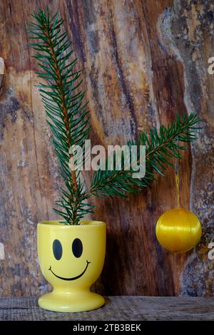 two fir fronds with single cheap hanging bauble sat in smiley face egg cup concept budget cost of living crisis christmas tree decoration Stock Photo