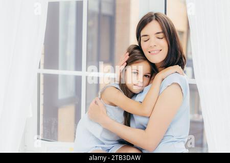 Content mother and child in a loving embrace by the window Stock Photo