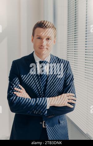 Confident businessman in a suit stands with crossed arms Stock Photo