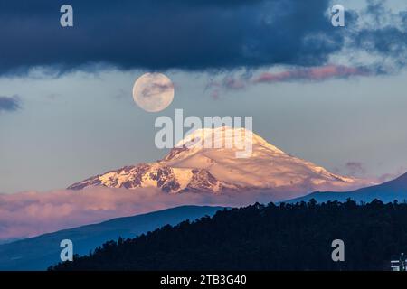 Cayambe volcano with the moon on one side at sunset seen from Quito, Ecuador Stock Photo