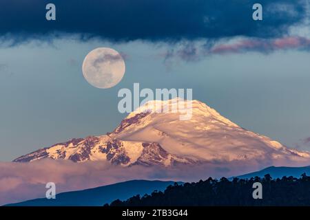 Cayambe volcano with the moon on one side at sunset seen from Quito, Ecuador Stock Photo