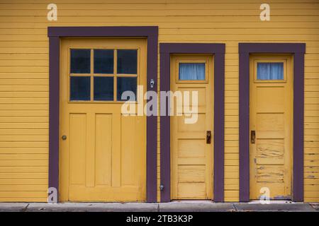 Close up of three doors on the side of a building where two are thinner and open opposite of each other. Stock Photo