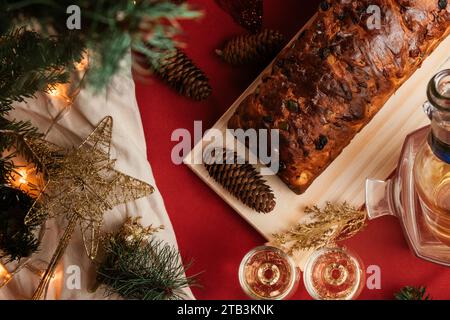 Top view of Yuletide cake featuring champagne, raisins, and dried fruits, placed on a red tabletop. cozy, warm, comforting Christmas decoration. Stock Photo