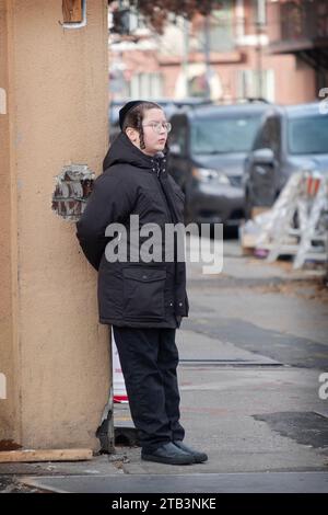 An orthodox Jewish boy with long curly peyus waits for friends while leanning up against a wall.. On Lee Avenue in Brooklyn, New York. Stock Photo