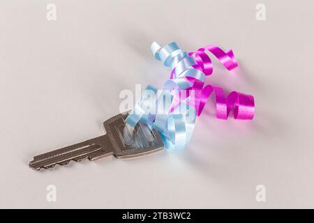 Key with pink and blue ribbon on a white surface. Copy space. Close up. Stock Photo