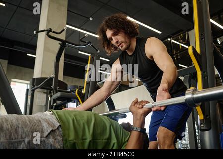Young caucasian athlete assisting unknown african american man doing bench press at gym Stock Photo